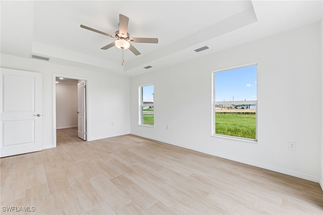 empty room with light wood-style floors, a tray ceiling, visible vents, and baseboards