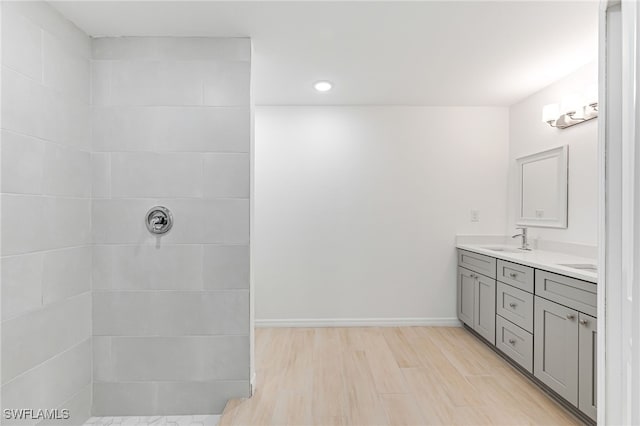 full bathroom with double vanity, baseboards, wood finished floors, a tile shower, and a sink