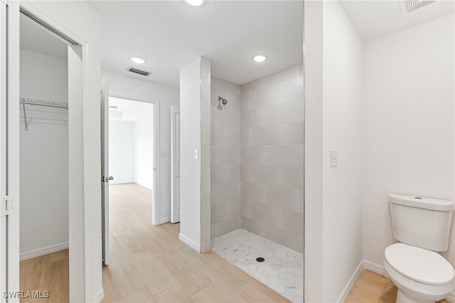 bathroom with visible vents, a tile shower, toilet, and wood finished floors