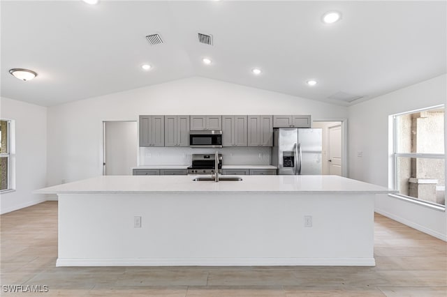 kitchen with lofted ceiling, gray cabinets, appliances with stainless steel finishes, a sink, and a large island with sink