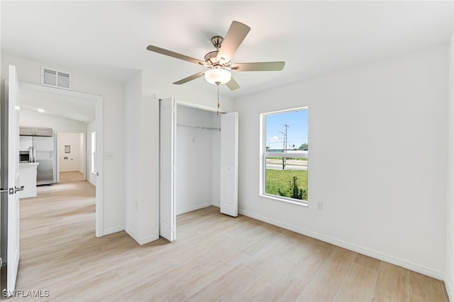 unfurnished bedroom featuring light wood-type flooring, stainless steel fridge, visible vents, and a closet