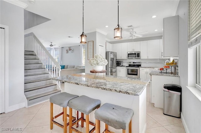 kitchen with light stone counters, light tile patterned floors, tasteful backsplash, appliances with stainless steel finishes, and a ceiling fan