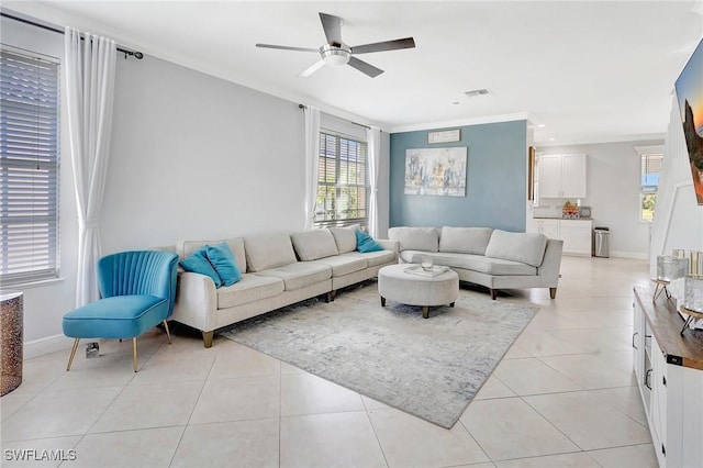 living area with light tile patterned floors, visible vents, ornamental molding, ceiling fan, and baseboards