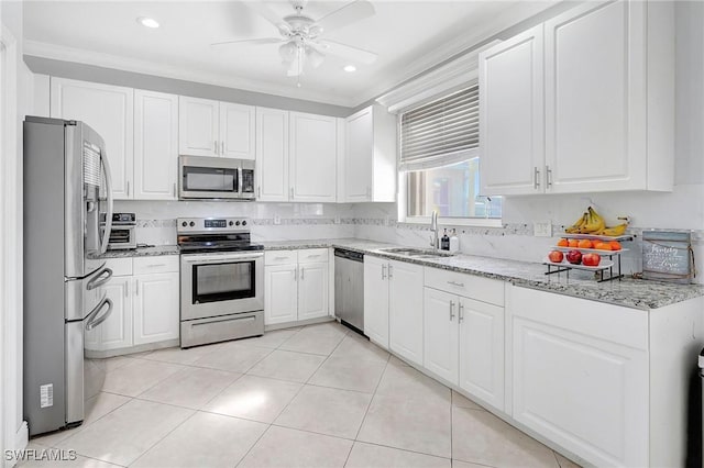 kitchen with appliances with stainless steel finishes, white cabinets, a sink, and light stone counters