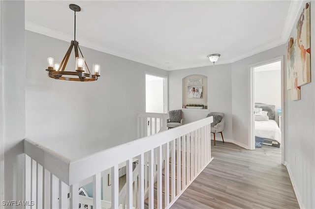 hall featuring ornamental molding, a notable chandelier, baseboards, and wood finished floors