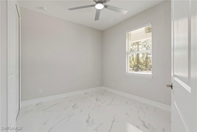 spare room with marble finish floor, ceiling fan, and baseboards