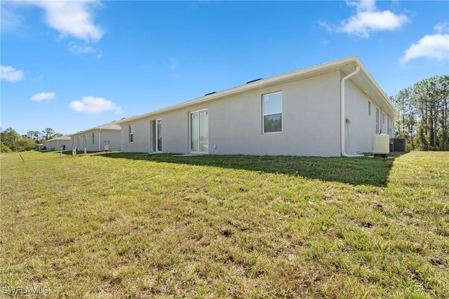 rear view of house with central air condition unit, a lawn, and stucco siding