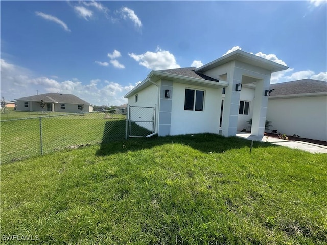 rear view of house featuring a gate, stucco siding, a yard, and fence