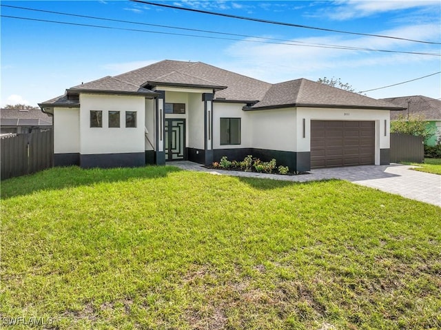 prairie-style home featuring an attached garage, fence, decorative driveway, stucco siding, and a front yard