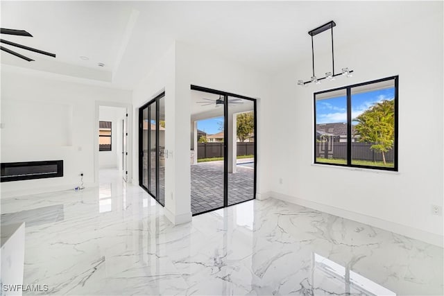 spare room with a healthy amount of sunlight, marble finish floor, baseboards, and a glass covered fireplace