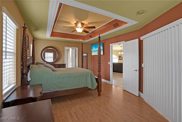 bedroom with wood finished floors, a raised ceiling, visible vents, and crown molding