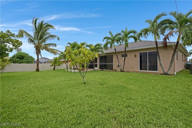 rear view of property with a yard, fence, and stucco siding