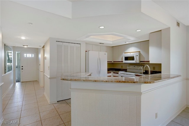 kitchen featuring light tile patterned floors, a peninsula, white appliances, light stone countertops, and tasteful backsplash