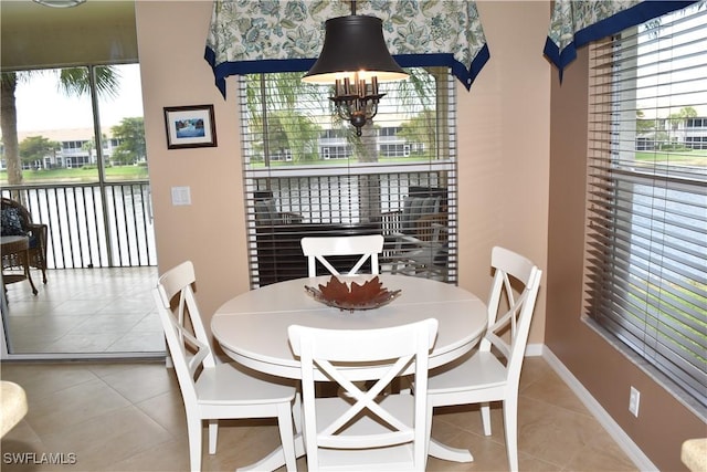 tiled dining area featuring a chandelier, a wealth of natural light, a water view, and baseboards