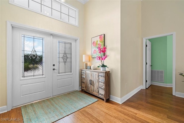 foyer with light wood finished floors, visible vents, a high ceiling, and baseboards