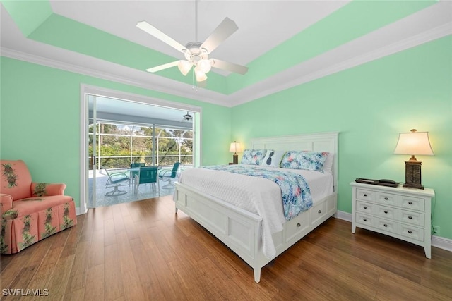 bedroom featuring access to exterior, a tray ceiling, and wood finished floors