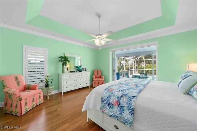 bedroom with access to exterior, a tray ceiling, crown molding, a sunroom, and wood finished floors