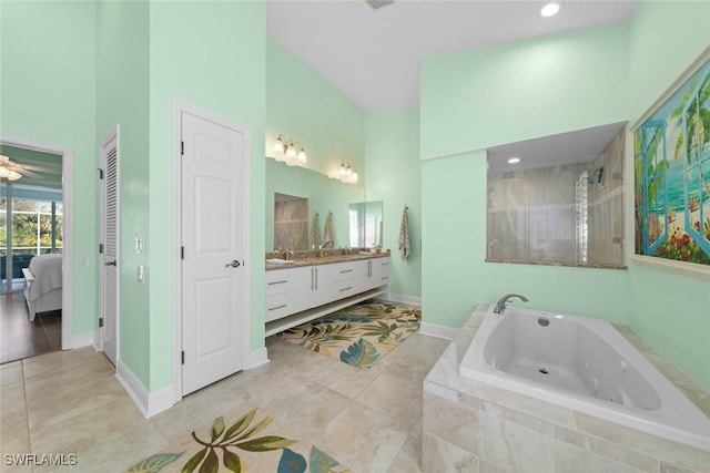 ensuite bathroom with a towering ceiling, vanity, tile patterned flooring, a whirlpool tub, and baseboards