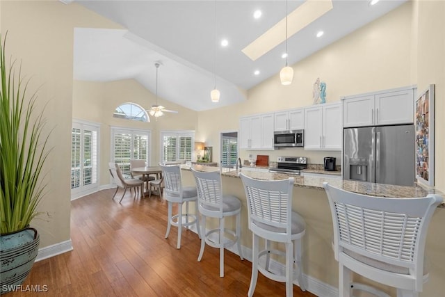 kitchen with a skylight, white cabinets, hanging light fixtures, appliances with stainless steel finishes, and hardwood / wood-style floors