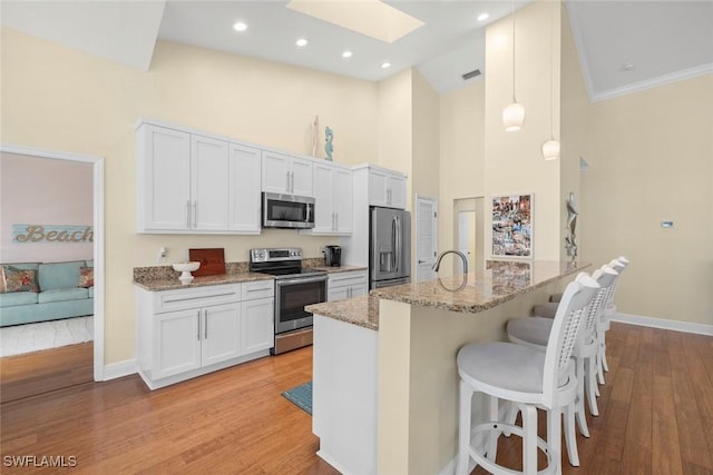 kitchen featuring a skylight, light wood finished floors, a kitchen breakfast bar, light stone countertops, and stainless steel appliances