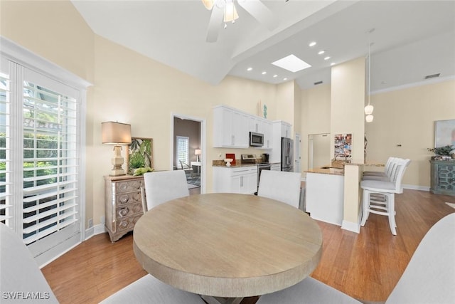 dining space with high vaulted ceiling, light wood finished floors, a skylight, and baseboards