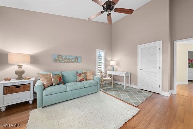 living area featuring a ceiling fan, wood finished floors, a towering ceiling, and baseboards