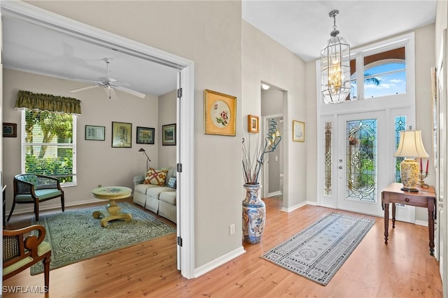 foyer with ceiling fan with notable chandelier, baseboards, and wood finished floors