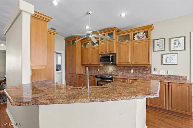 kitchen with stone counters, stainless steel appliances, backsplash, a sink, and a peninsula