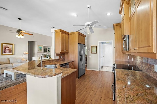 kitchen with appliances with stainless steel finishes, light wood-style floors, open floor plan, a sink, and a peninsula