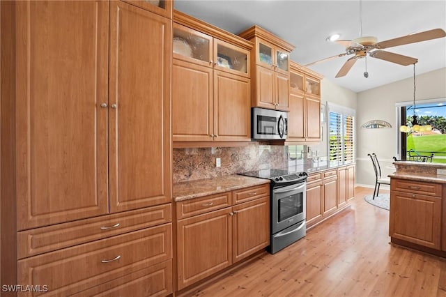 kitchen featuring light stone counters, light wood finished floors, decorative backsplash, appliances with stainless steel finishes, and ceiling fan