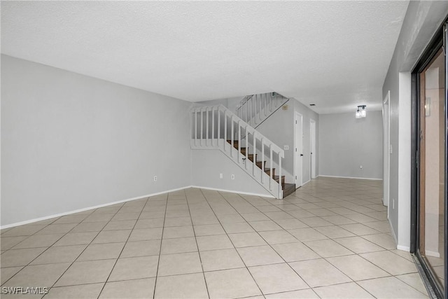 spare room featuring a textured ceiling, light tile patterned floors, stairway, and baseboards