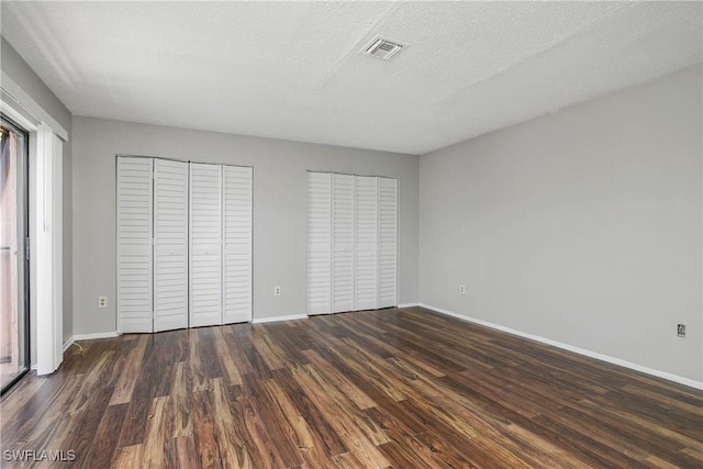 unfurnished bedroom featuring two closets, visible vents, dark wood-type flooring, a textured ceiling, and baseboards