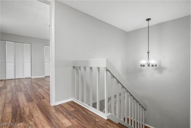 stairway featuring a notable chandelier, baseboards, and wood finished floors