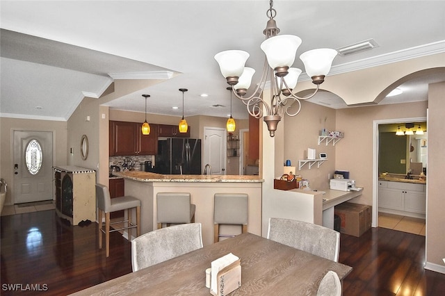 dining area with arched walkways, a notable chandelier, wood finished floors, visible vents, and crown molding