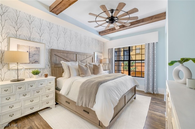 bedroom with an accent wall, wood finished floors, a ceiling fan, beam ceiling, and wallpapered walls