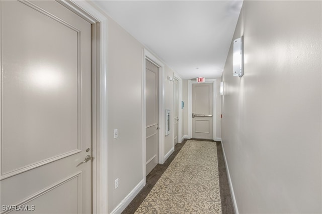 hall featuring dark carpet and baseboards