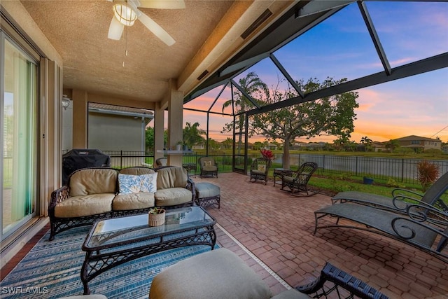 patio terrace at dusk with a lanai, outdoor lounge area, area for grilling, fence, and a ceiling fan