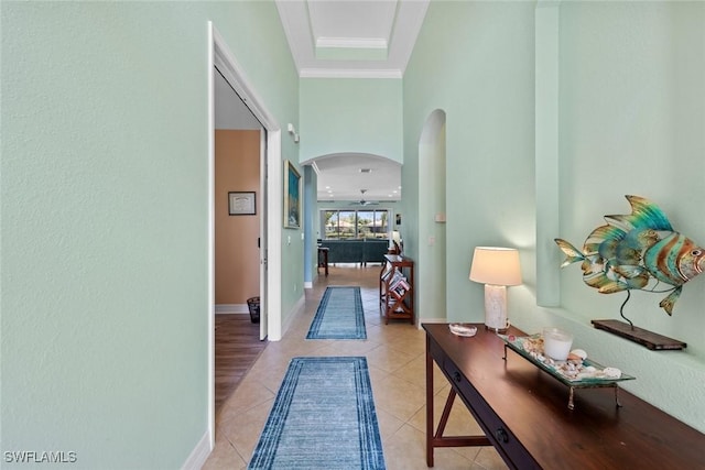 hall with light tile patterned floors, baseboards, arched walkways, and crown molding