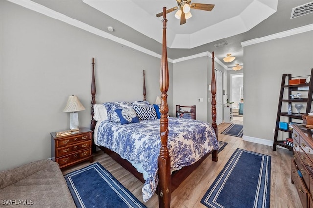 bedroom featuring ornamental molding, a tray ceiling, visible vents, and light wood-style flooring