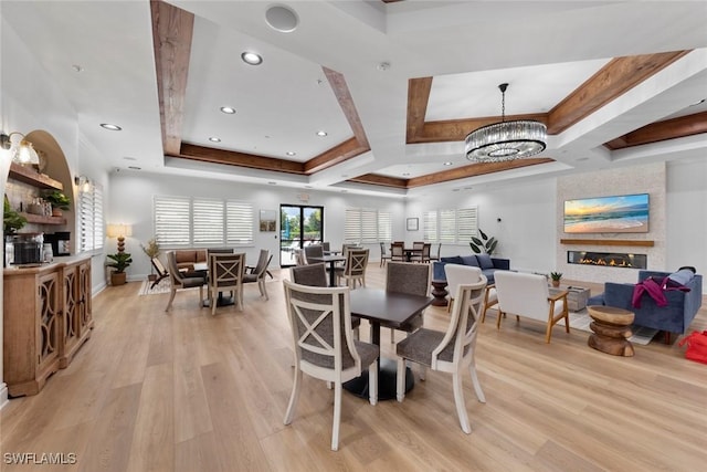 dining space featuring a notable chandelier, recessed lighting, a raised ceiling, a large fireplace, and light wood-type flooring