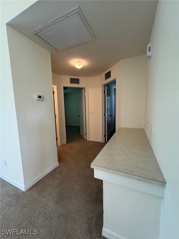 corridor featuring baseboards, visible vents, and dark colored carpet