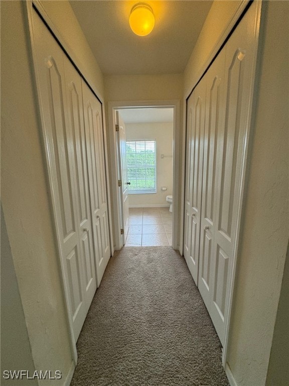 hallway with light carpet, light tile patterned floors, and baseboards