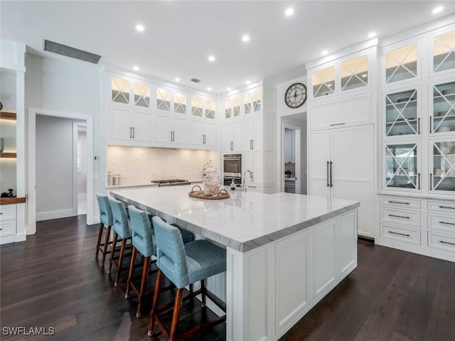 kitchen featuring light stone counters, white cabinets, a large island, decorative backsplash, and dark wood-style floors