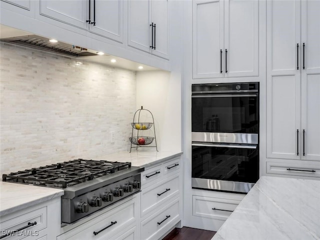 kitchen featuring stainless steel appliances, white cabinetry, light stone counters, and decorative backsplash