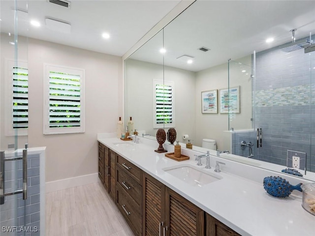 bathroom with toilet, a shower stall, double vanity, and a sink