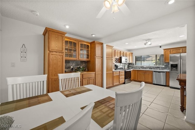 kitchen featuring stainless steel appliances, tasteful backsplash, glass insert cabinets, light tile patterned flooring, and a sink