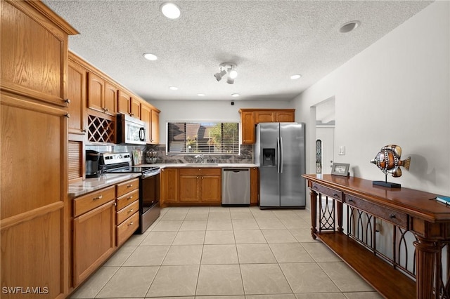 kitchen with light tile patterned floors, stainless steel appliances, light countertops, backsplash, and a sink