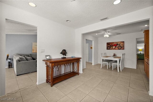 hall with a textured ceiling, light tile patterned flooring, visible vents, and recessed lighting