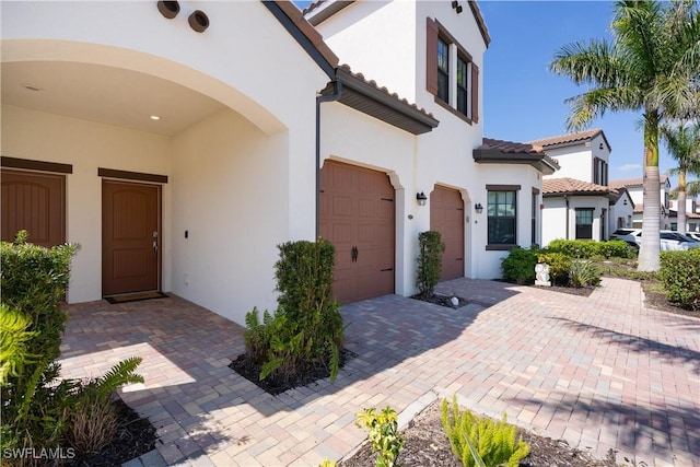 view of front of home with decorative driveway, a tile roof, an attached garage, and stucco siding