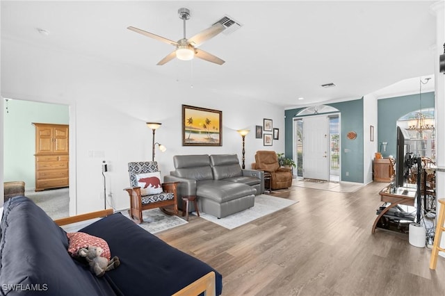 living area featuring ceiling fan with notable chandelier, wood finished floors, visible vents, and baseboards